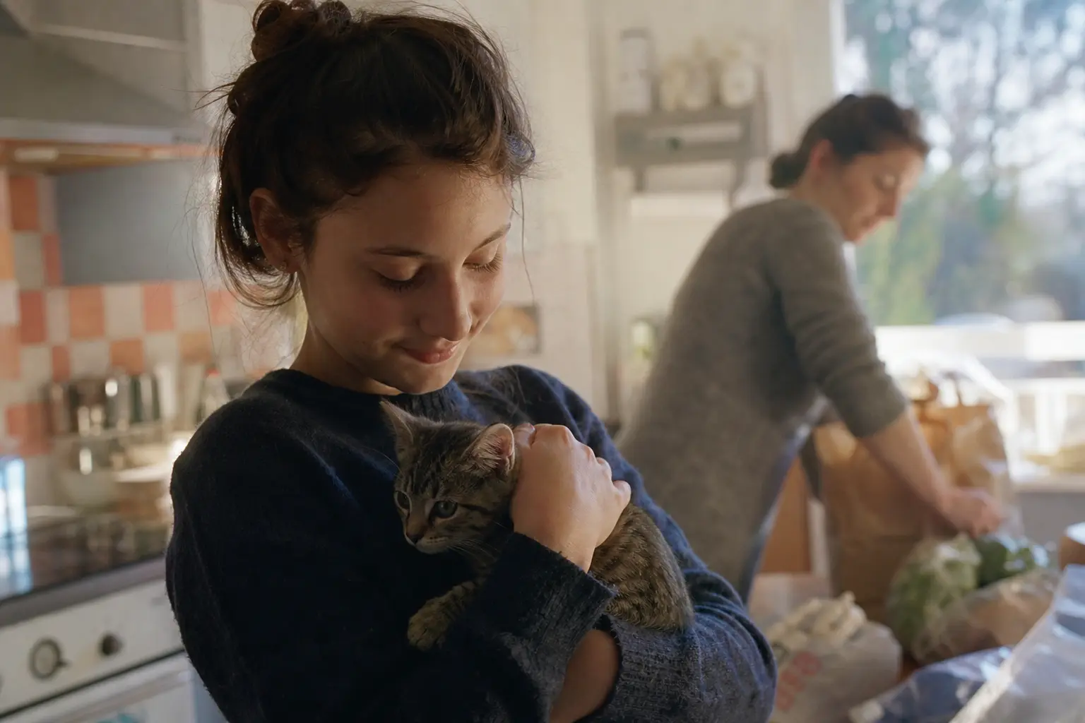Une adolescente tient un chaton de huit semaines dans une cuisine familiale