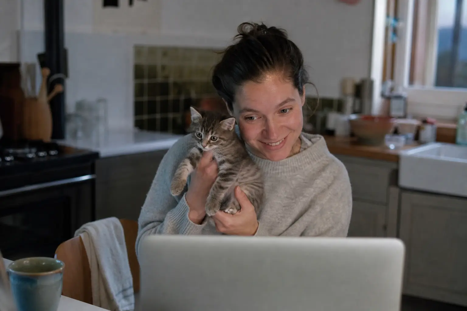 Une femme montre son chaton à la caméra de son téléphone pendant une téléconsultation vétérinaire dans son salon