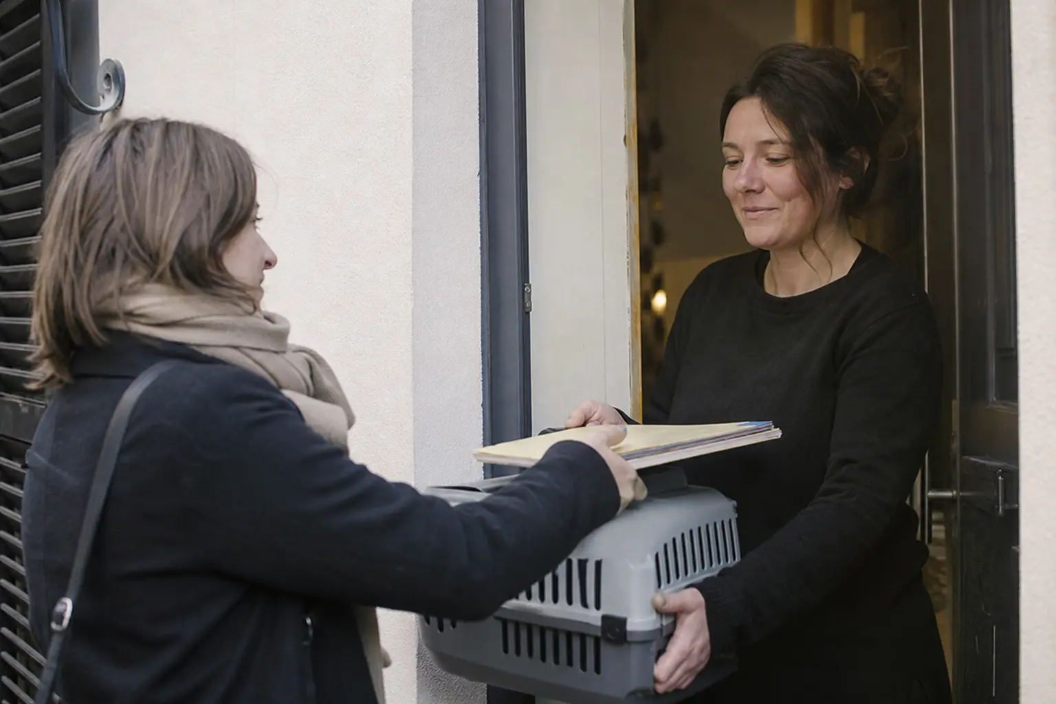 Deux personnes se transmettent une caisse de transport contenant un chat devant une porte d'entrée