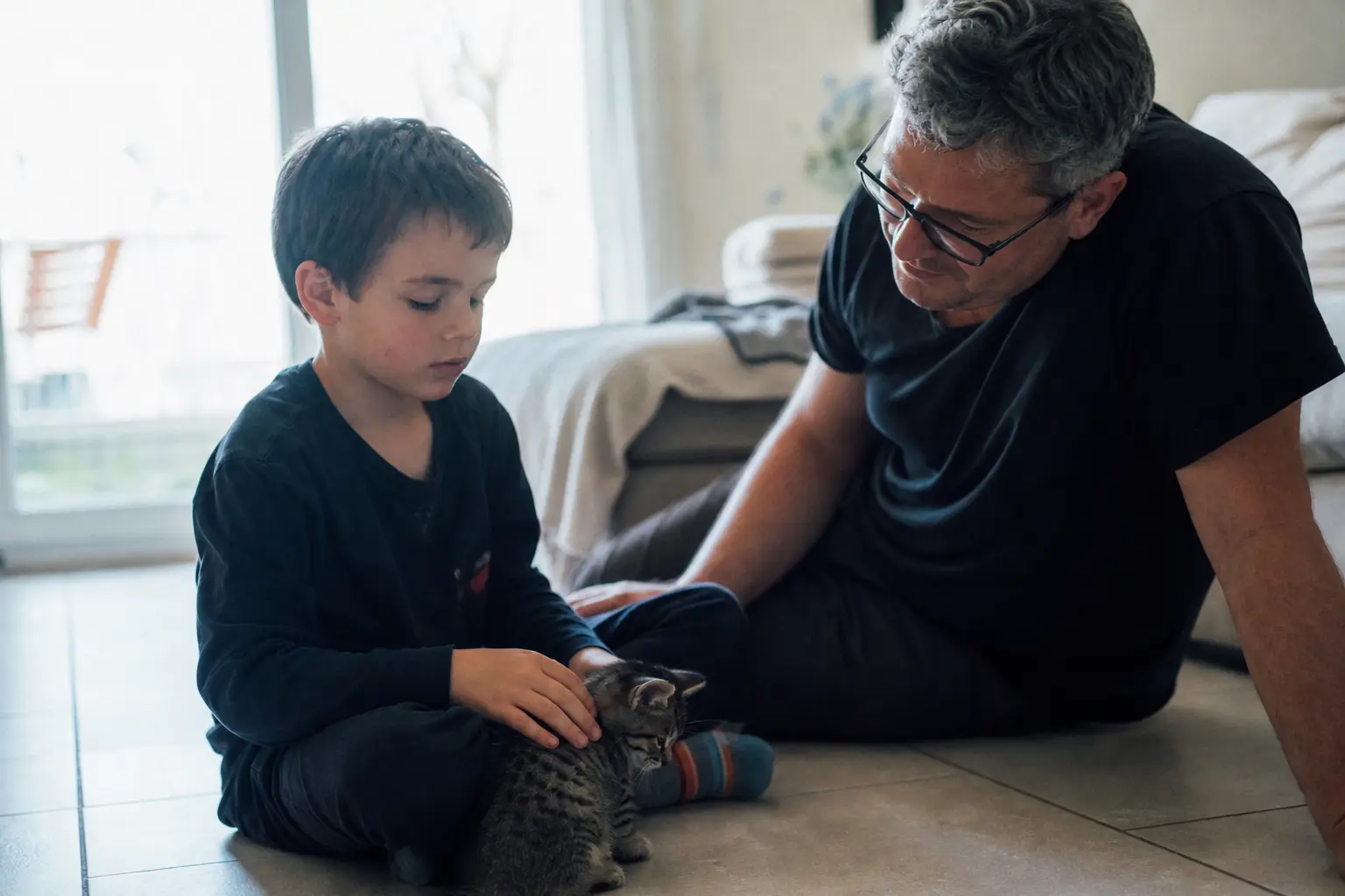Un enfant de six ans caresse doucement un chaton sous le regard attentif d'un adulte