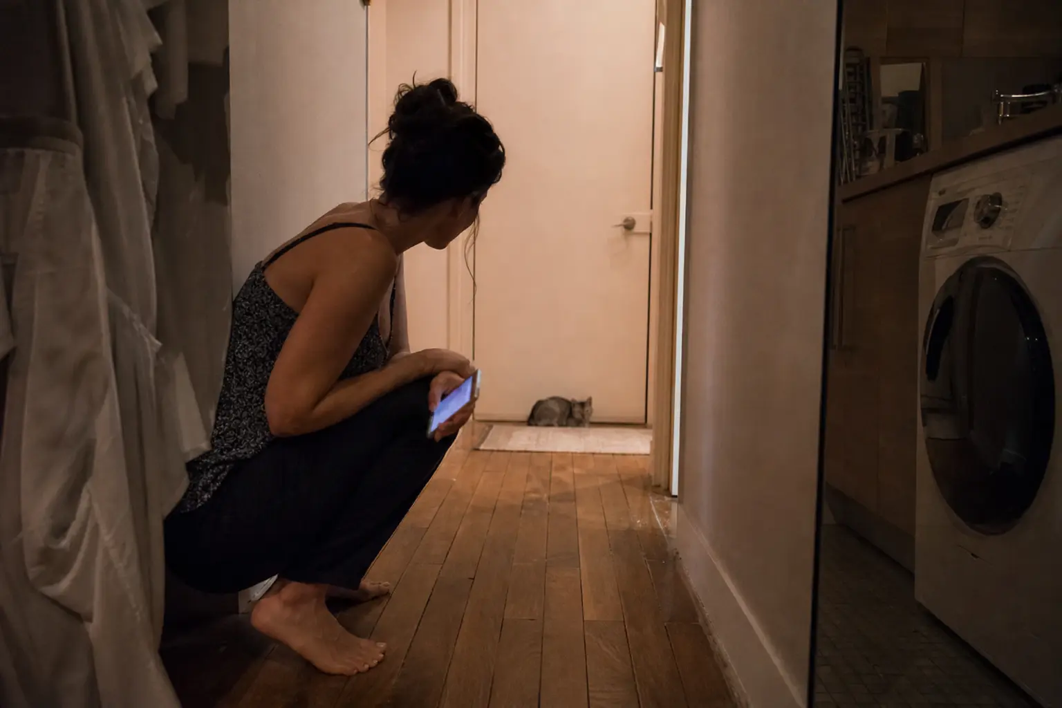 Une femme observe attentivement son chaton prostré dans un couloir d'appartement