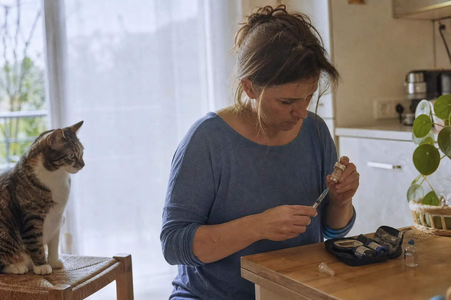 Une femme prépare une seringue d'insuline sur un plan de travail de cuisine, un chat attend à côté