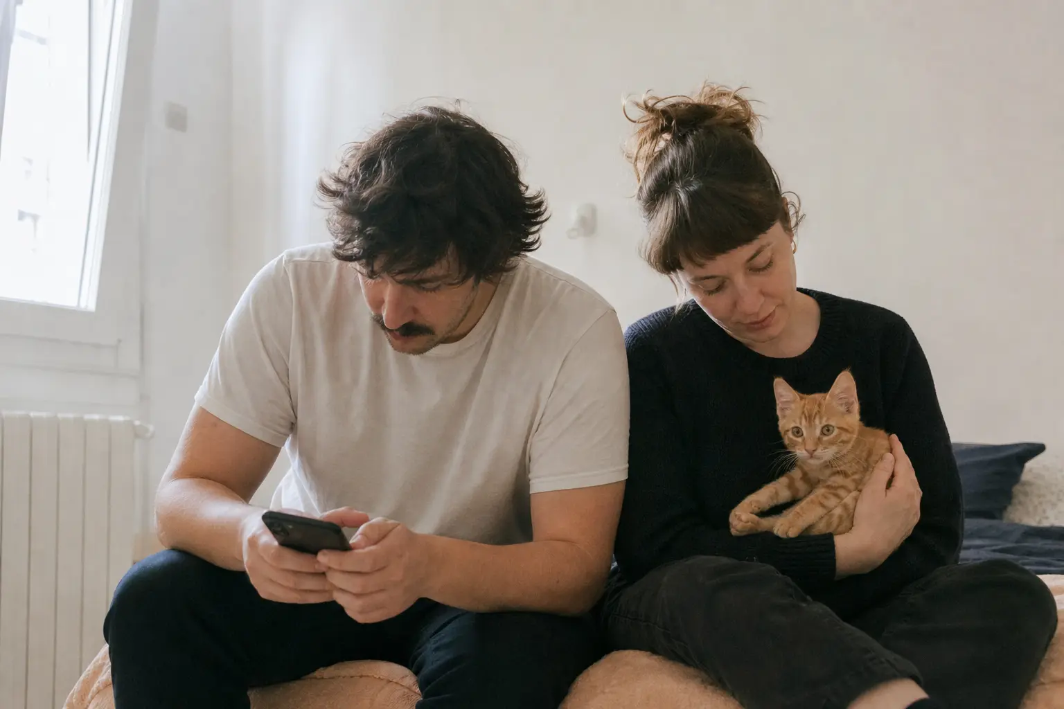 Un couple assis sur un lit consulte un téléphone, l'un d'eux tient un chaton roux